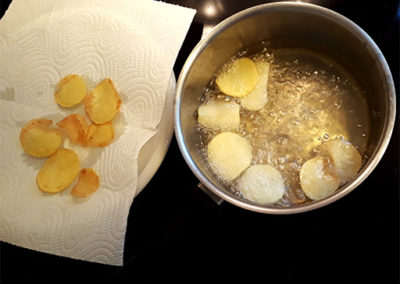 Chips i kogende olie og chips som ligger til tørring på køkkenrulle ved siden af